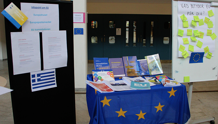 Bokbord, utställningsskärmar och EU-flaggor i gymnasiets ljushall